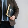 Business professional in a suit holding various folders and notebooks indoors.